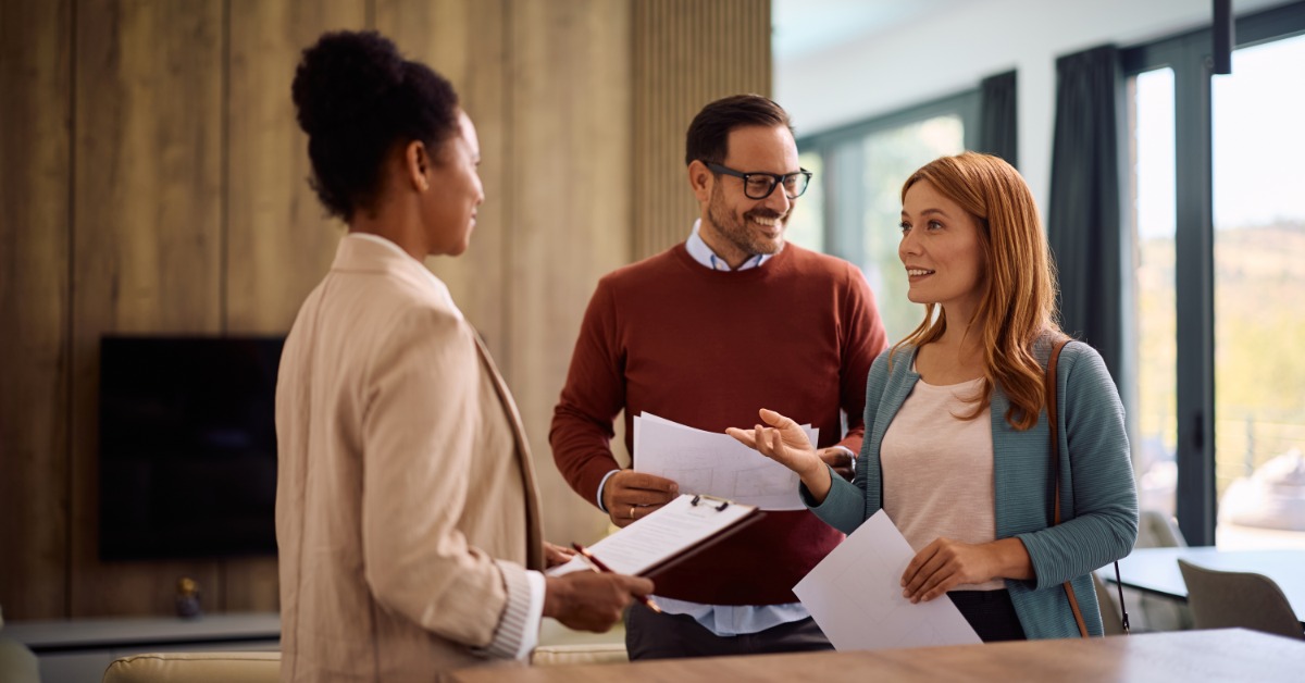 A real estate agent reviews property documents with two clients inside a bright, modern residential home.