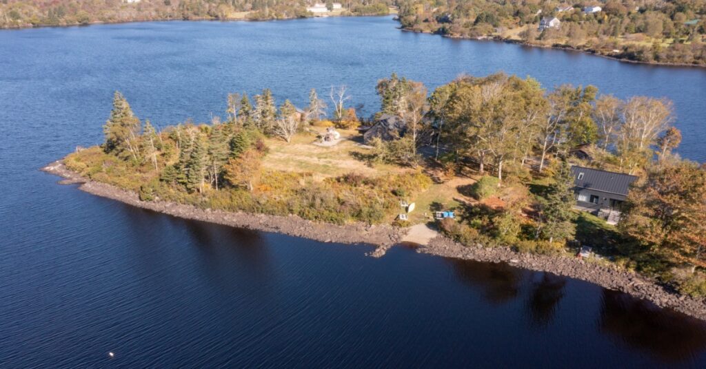 An aerial view shows a wooded waterfront property extending along the shoreline of a large blue lake.