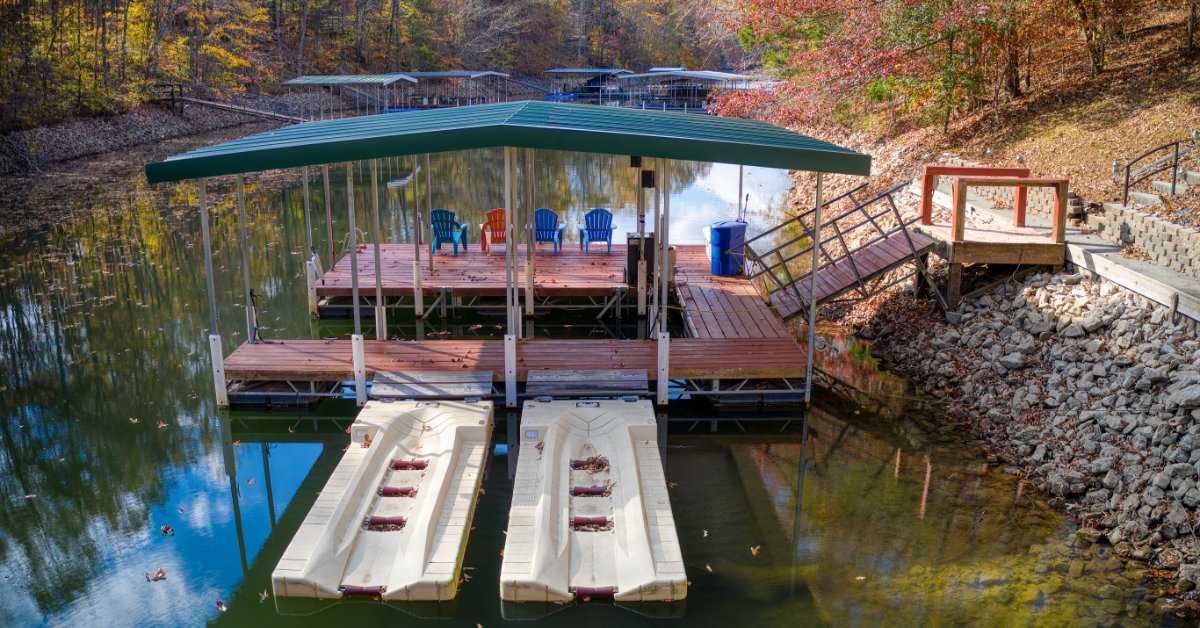 A covered private boat dock with two empty boat lifts sits along a rocky shoreline surrounded by autumn trees.