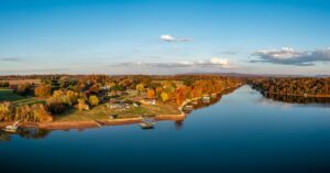 An aerial view shows homes and private docks along a wooded lake shoreline surrounded by autumn foliage.