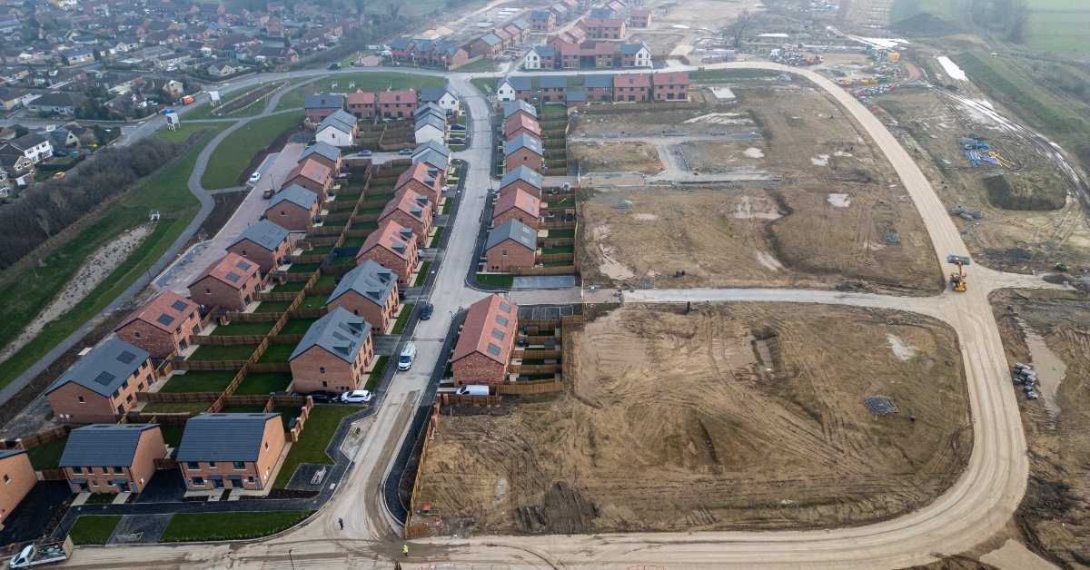 An aerial view shows undeveloped land beside an established residential neighborhood and new construction.