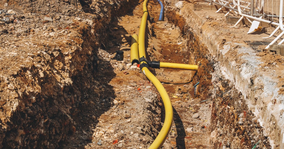 Yellow utility conduit runs through an excavated trench at a construction site surrounded by exposed soil.